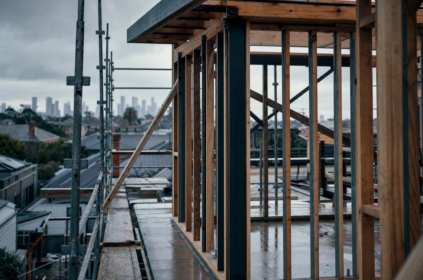 A Melbourne residential construction site with exposed timber wall framing and scaffolding under a grey sky